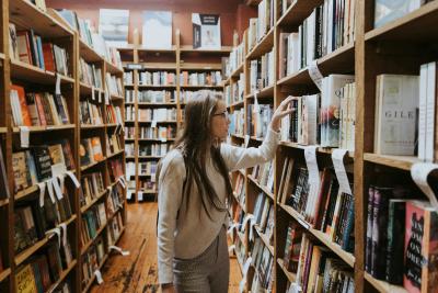 Photo of woman reaching for a book in a library by Becca Tapert on Unsplash